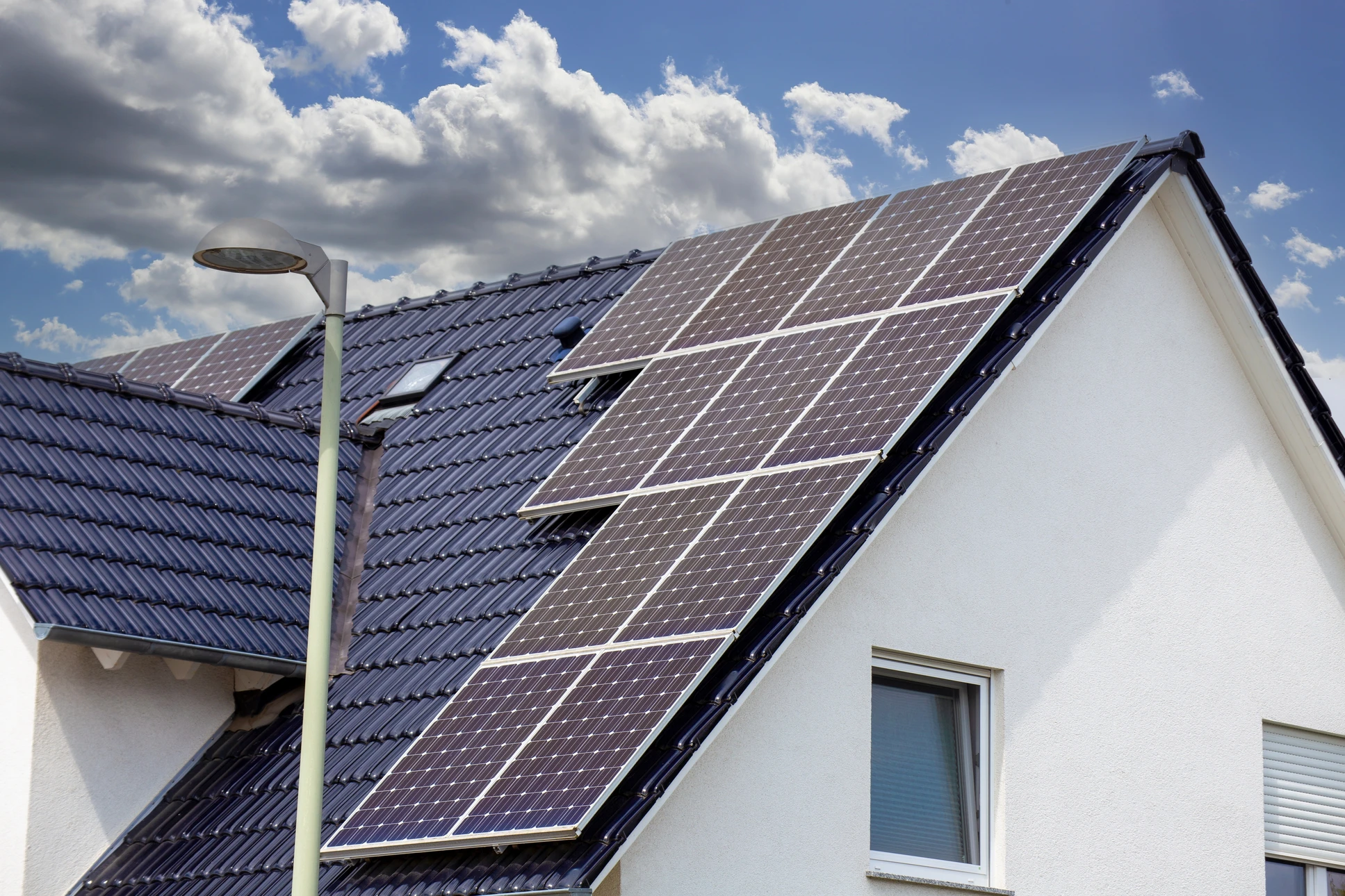 Deux techniciens installent des panneaux photovoltaïques sur une toiture en tuiles rouges
