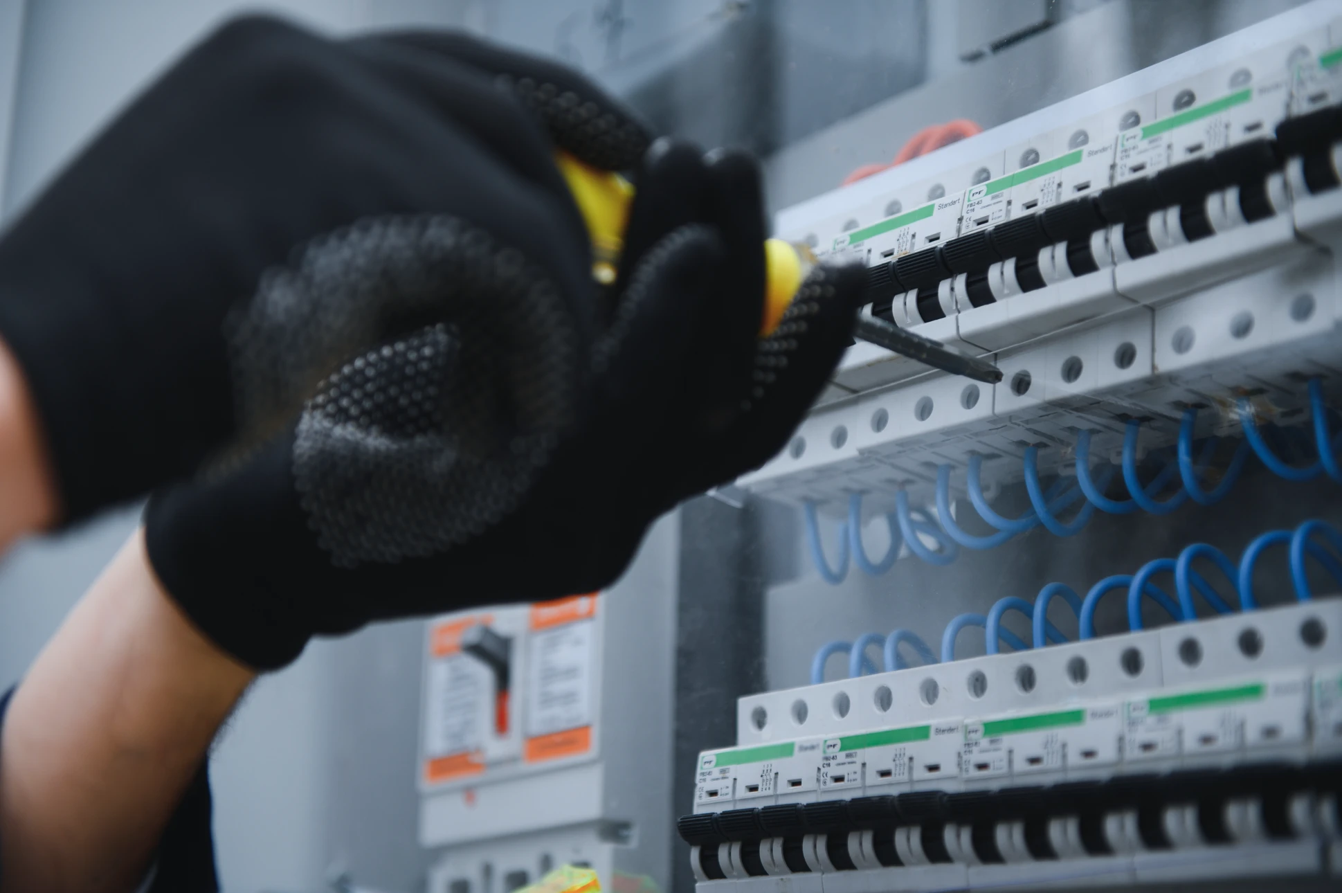 Électricien professionnel en combinaison travaillant sur un tableau électrique industriel, testant les circuits avec un multimètre